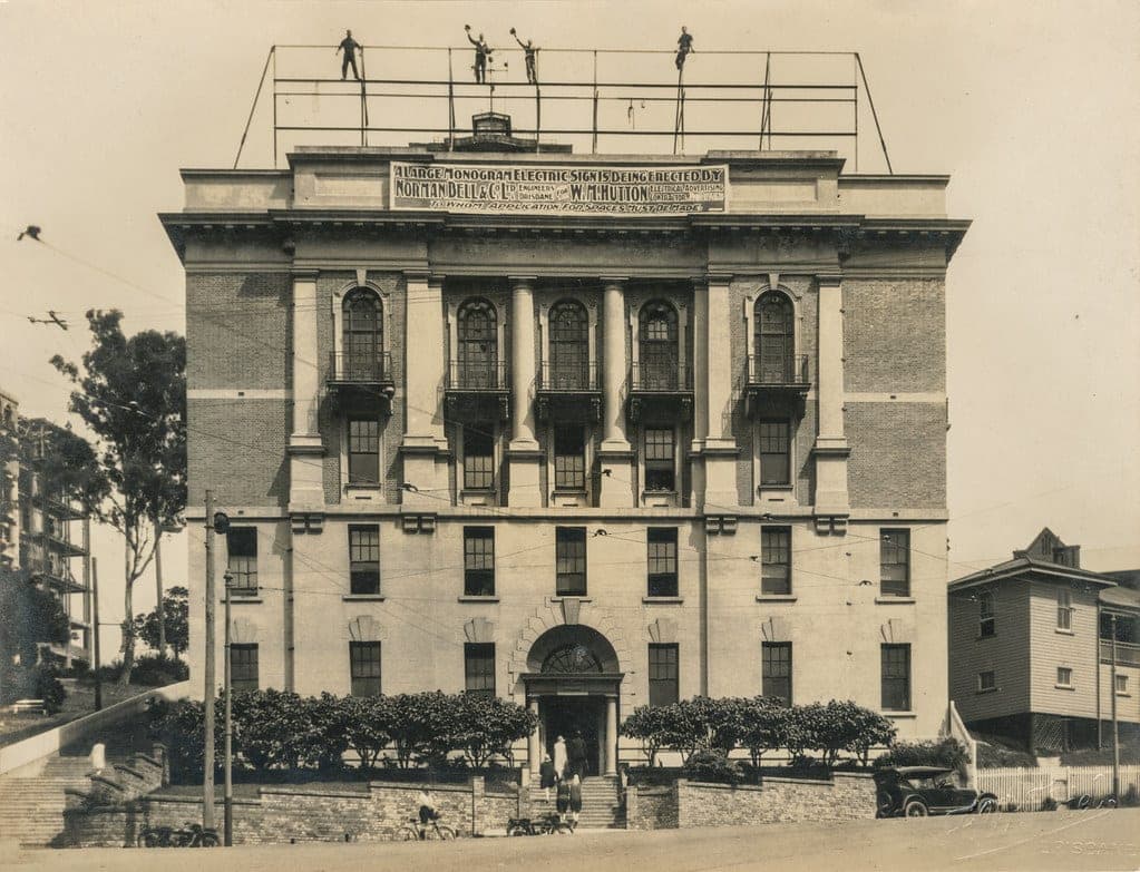 Workers waving from the metal support structure before an electric sign was installed atop Brisbane Trades Hall in Turbot Street in 1928